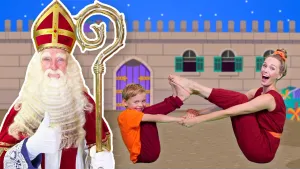 Een foto van de presentator die samen met een jongetje in een yogahouding op de grond zit. Ze hebben de achterkant van hun voeten tegen elkaar aan en houden elkaars handen vast. Op de voorgrond is Sinterklaas te zien en op de achtergrond een kasteelmuur.