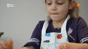 Een foto van een kind dat met veel aandacht kijkt naar iets in haar handen. Ze heeft een schort aan.