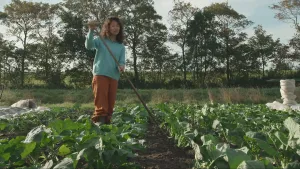 Een foto van presentator Serah die in een tuin tussen de planten staat met tuingereedschap in haar hand.