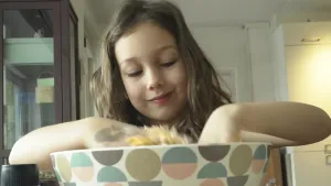 Een foto van een meisje die met haar handen in een schaal zit met eten erin.