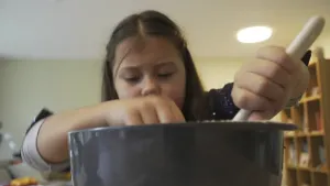 Een foto van een meisje die in een pot staat te roeren.