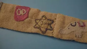 Een foto van een deel van een riem van stof gemaakt door het Joodse meisje Leontien. Op de foto zijn enkele sysmbolen die op de riem genaaid zijn te zien, het symbool van de Jodenster en een circusolifant.