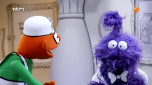 Een foto van twee gekleurde poppen in een zwart-witte kamer. De oranje pop praat tegen de paarse pop, en de paarse pop kijkt naar de grond.