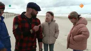 Een foto van presentator Tim die op het strand staat met drie kinderen. Het is erg bewolkt.