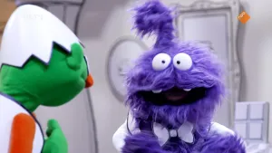 Een foto van twee gekleurde poppen in een zwart-witte kamer. De groene pop kijkt naar de paarse pop. en de paarse pop kijkt naar de kijker.