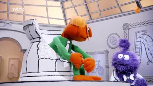 Een foto van twee gekleurde poppen in een zwart-witte kamer. Alle dingen in de kamer hebben zwarte lijntjes, alsof ze getekend zijn. De oranje pop zit op een stoel en kijkt naar de paarse pop.