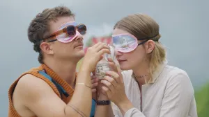 Een foto van presentatoren Emma en Jurre die met blinddoeken op een geopend potje vasthouden en erin ruiken.