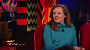 Een foto van een vrouw die in de studio zit van Eus’ Boekenclub. Op de achtergrond is er een man zichtbaar van het publiek.