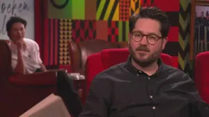 Een foto van een man die in de studio zit van Eus' Boekenclub. Op de achtergrond zit er een man van het publiek.