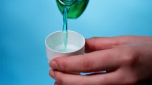 Een foto van een hand die een beker vasthoudt terwijl er met een fles  mondwater ingegoten wordt.