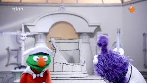 Een foto van een groene pop en een paarse pop die kijkt naar de groene pop. Ze staan voor een kapotte pot in het museum van gewone dingen.