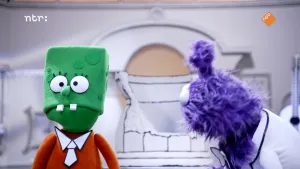 Een foto van twee gekleurde poppen in een zwart-witte kamer. Alle dingen in de kamer hebben zwarte lijntjes, alsof ze getekend zijn. De groene pop heeft op zijn kleding een stropdas die ook zo getekend is.