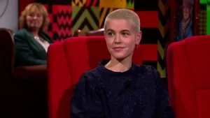 Een foto van een vrouw die op een rode stoel zit in de studio. Achter haar zit een vrouw die toekijkt.