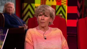 Een foto van een vrouw die op een rode stoel in de studio zit. Op de achtergrond zit er nog een vrouw die toekijkt.