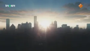 Een foto van een stad met een lage zon in het midden van het beeld. Er zijn weinig wolken in de lucht.