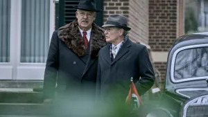 Een foto van twee mannen die over straat langs een auto lopen met nazi-vlaggetjes. 