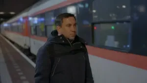 Een foto van een man die naast een trein staat op het perron van een treinstation. 