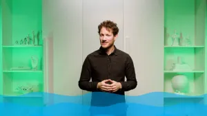 Een foto van een presentator voor een dichte, witte kast. Onderaan de foto zijn blauw getekende golven zichtbaar. 