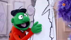 Een foto van een groene pop die een steen van piepschuim vasthoudt. Hij praat met een paarse pop rechts in beeld.