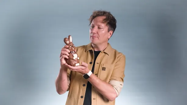 Een foto van een presentator die een paashaas van chocolade vastheeft en ernaar kijkt.
