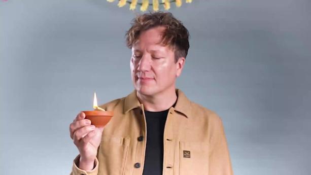 Een foto van presentator Klaas met een kaarsje in zijn hand. Hij kijkt naar de kaars. De kaars is een klein bruin kommetje met een lont die erboven uitsteekt..