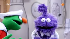 Een foto van twee gekleurde poppen in een zwart-witte kamer. De groene pop kijkt naar de paarse pop, en de paarse pop kijkt naar de grond.