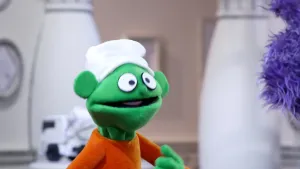 Een foto van een groene pop die met een paarse pop praat in het museum van gewone dingen. Rechts is alleen het gezicht te zien van de paarse pop.