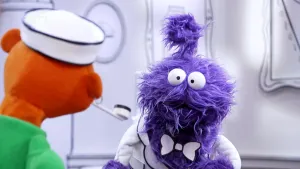 Een foto van het achterhoofd van een oranje pop in het museum van gewone dingen. Hij kijkt naar een paarse pop die terug kijkt.