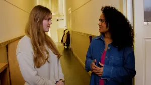 Een foto van presentator Ciana die met een vrouw praat in de gang van een school.