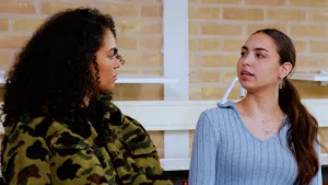 Een foto van presentator Ciana die met een vrouw staat te praten in de gang van een school.