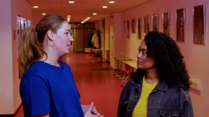 Een foto van presentator Ciana die praat met een vrouw terwijl ze in een gang staan van een school.