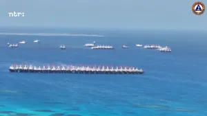 Een foto van de zee waar een groot aantal schepen zij aan zij naast elkaar in water liggen. Op de achtergrond zijn er nog meer schepen zichtbaar die zij aan zij liggen.