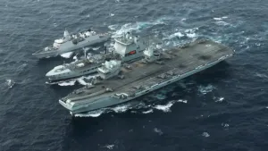 Een foto van boven genomen van drie marine schepen die in de zee varen. Een van de schepen is een vliegdekschip.