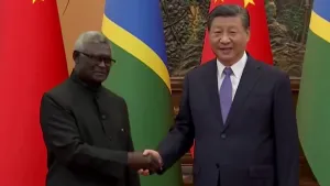 Een foto van de Chinese president Xi Jinping die de hand schudt met een leider van een land. Op de achtergrond zijn vlaggen van landen te zien waaronder die van China.