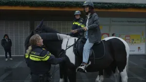 Een foto van twee politiepaarden op straat. Presentator Serah zit op het voorste paard. Op het andere paard zit een agent. Een tweede agent houdt het paard van de presentator vast.