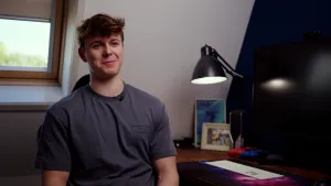 Een foto van een jongen, Fons Ellinga aan een bureau op zolder. Op het bureau ligt een toetsenbord en staan een monitor, kleine luidsprekers en een bureaulamp. Ook liggen er twee controllers om te gamen op het bureau.
