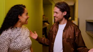 Een foto van presentator Ciana. Ze praat enthousiast met gast Jasper. Ze staan in een smalle gang.