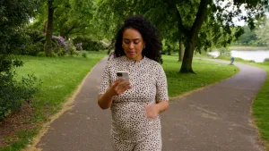 Een foto van presentator Ciana die loopt in een park. Ze kijkt naar haar mobiele telefoon.