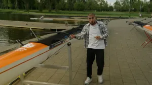 Een foto van presentator Nizar die naast een boot staat die aan land op een standaard ligt. Op de achtergrond ligt er nog een boot op een standaard.