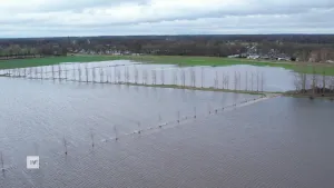 Een foto van een landschap waar verschillende weides onder water staan. Er lopen twee paden tussen de weides die ook deels onder water staan. 