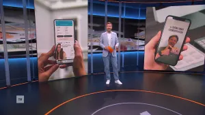 Een foto van presentator Rob Hadders in de  studio. Hij staat tussen twee schermen waarop telefoons te zien zijn. Op een van de telefoons wordt een influencer getoond.