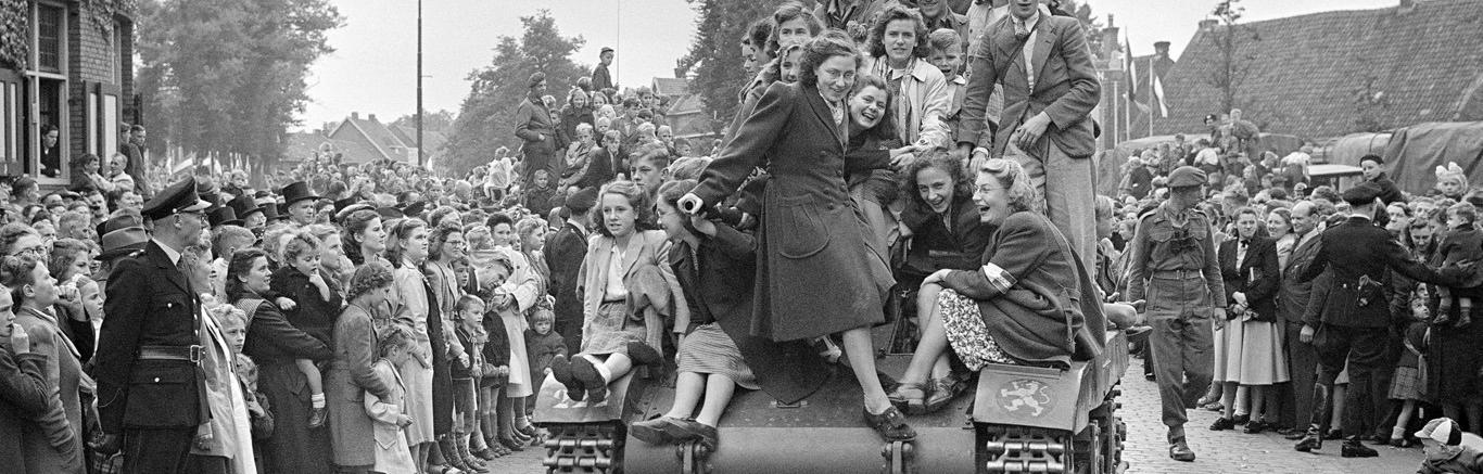 Zwart-witfoto van blije mensen op straat en op een tank.