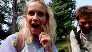 Een foto van presentatoren Janouk en Bram met op de achtergrond bomen. Janouk kijkt blij verrast met open mond en Bram lacht en kijkt naar beneden.