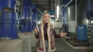 Een foto van presentator Janouk die middenin een drinkwater zuivering bedrijf staat.