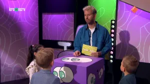 Een foto van de presentator bij een grote doos met ogen erop. Rond de doos staan drie kinderen die naar de presentator kijken. Hij praat tegen ze.