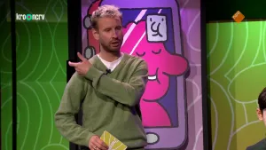 Een foto van de presentator, die met een hand over zijn schouder gebaart. Achter hem hangt een tekening van een smartphone met een gezicht op het scherm.