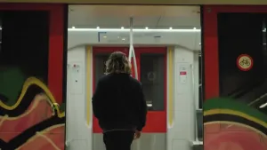 Een foto van presentator Pascal die met zijn rug naar de camera in de Amsterdamse metro staat. De deuren van de metro staan nog open.