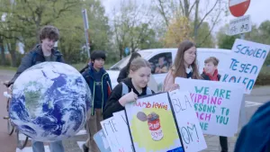 Een foto van kinderen die met protestborden lopen om te demonstreren. Op de borden staan teksten als "Scholen tegen kolen". Een jongen houdt een grote opblaasversie van de wereldbol vast.