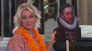 Een foto van presentatrice Janouk die in haar handen een portet van Willem van Oranje op een stok vastheeft. Ook draagt Janouk een oranje slinger om haar nek en een blouse met oranje bloemen.