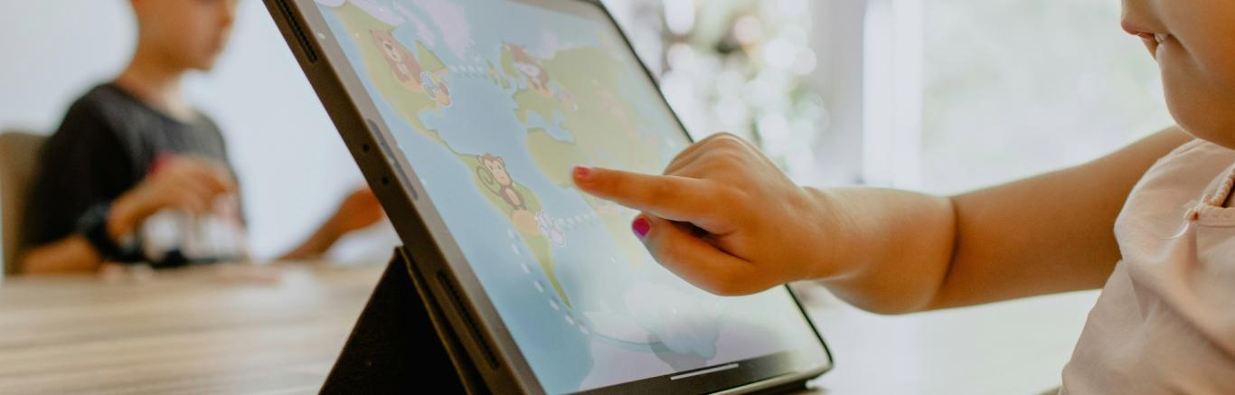 Kind speelt aardrijkskundig spelletje op tablet en wijst iets aan met vinger. Photo by Kelly Sikkema on Unsplash.